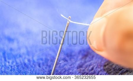 A Hand Trying To Pass A Thread Strand Through The Eye Of A Needle