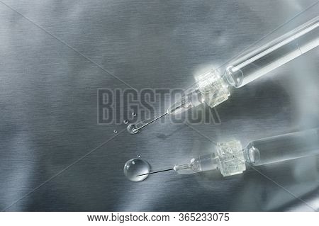 Close-up Of Two Syringes With A Luer Lock With Needles And Drops Of Injections Leaking On A Silver B