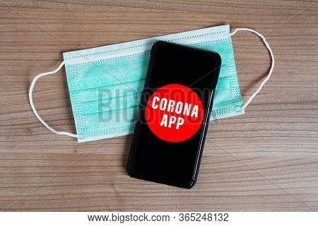Mock-up Corona App On Smartphone Or Mobile And Face Mask On Desk - Fictive Coronavirus Covid-19 Mobi