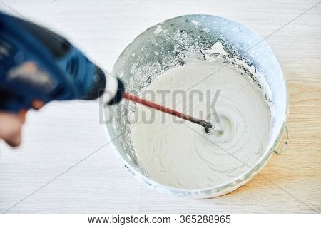 Worker Mixing Plaster In A Bucket For Alignment And Putty Walls Of The Apartment Using An Electric D