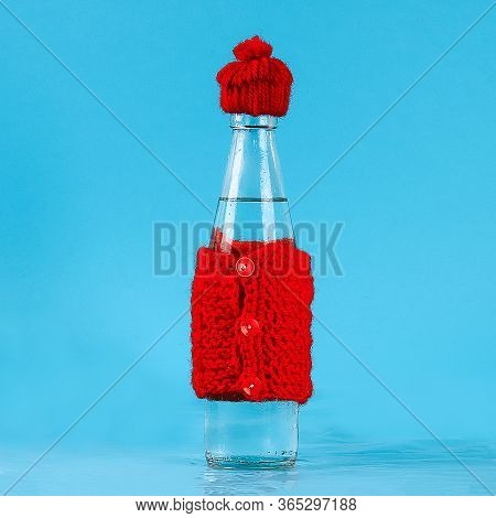 A Glass Bottle With Cold Water Is Dressed In A Hat And A Warm Jacket. The Concept Of Heat And Frost.