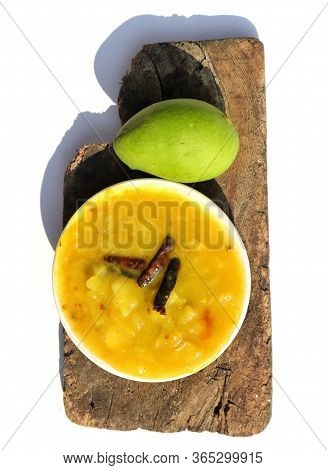 Mango Chutney In A Plate With A Raw Mango On Wooden Piece With White Background