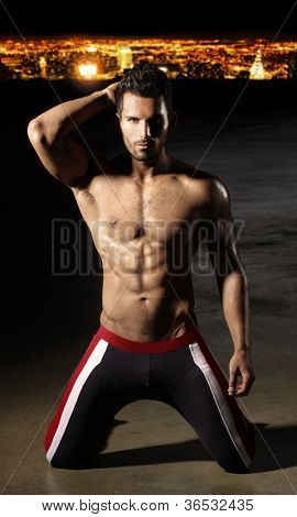 Bonne recherche bodybuilder sexy posant dans la nuit contre les lumières de la ville en arrière-plan