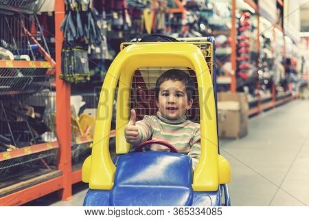 The Boy Is 4 Years Old In A Construction Shop, Sitting In A Cart. Toned