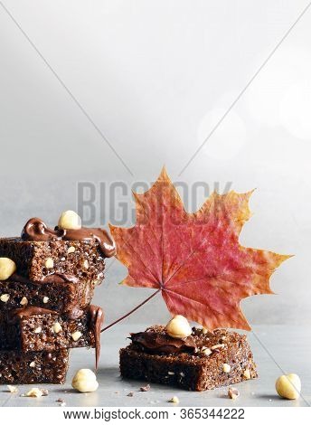 Stack Of A Brownie Pieces With Hazelnut And Leaf On A Grey Table With Gray Background.