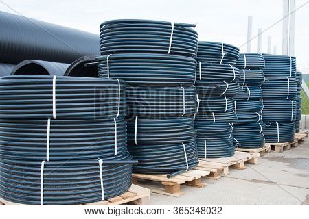 A Lot Of Rolled Plastic Pipes. Stock, Preparation For Laying. Rolls Of Black Pipes In The Open.