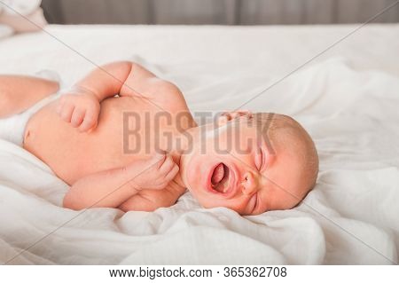 Newborn On The Bed. Crying, Screaming Baby Close Up And Copy Space. Baby Smile And Colic In Newborns