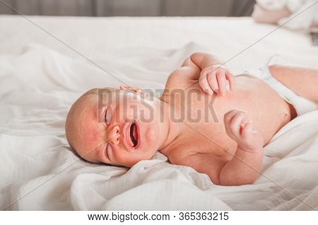 Newborn On The Bed. Crying, Screaming Baby Close Up And Copy Space. Baby Smile And Colic In Newborns