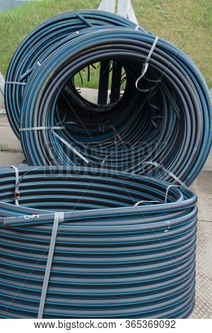 A Lot Of Rolled Plastic Pipes. Stock, Preparation For Laying. Rolls Of Black Pipes In The Open.