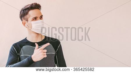 Young Confident Sports Man In Medical Face Mask Pointing With Finger To Background With Copy Space. 