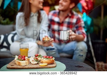 focus on sandwiches with cherry tomato and orange juice with couple in the background out oif focus talking, smiling. People, food and beverage