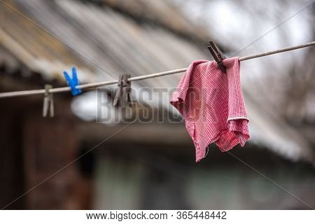 A Red Cleaning Cloth Dries On A Rope In The Courtyard Of A Village House. Clips For Linen. Hand Wash