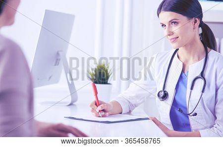Doctor and patient discussing medical problems in a hospital consulting room. Doc filling in a patient's form