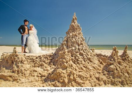 En ung och vacker nyligen gift par njuter på stranden nära sand slott vid havet kanten