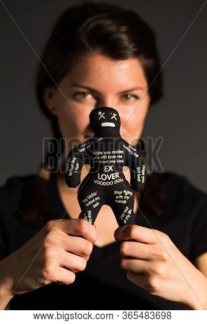 Woman Holding A Black Voodoo Doll By Its Legs In Her Hands