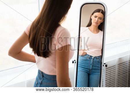 Weight Gain. Unhappy Girl Touching Drooping Belly Standing In Front Of Mirror At Home. Empty Space, 