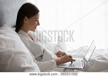 Woman Lying In Bed Using Laptop Check Email In Morning