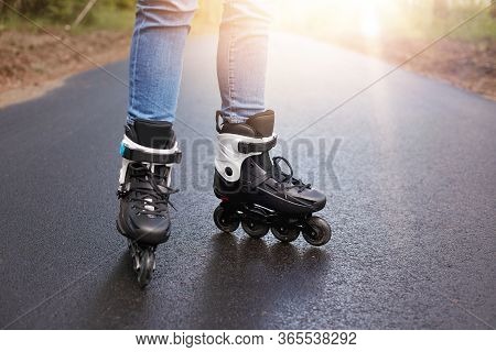 Horizontal Picture Of Unknown Person Rollerskating, Rollerskates Being On Wet Road, Having Sun On Ba