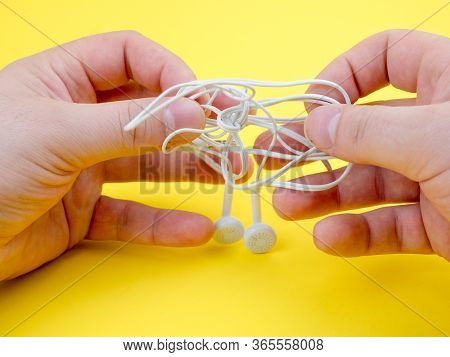 Man Untangles Headphones, On A Yellow Background. Close Up.
