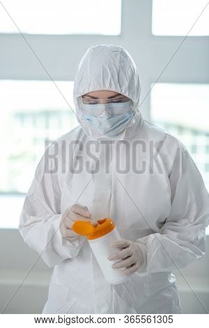 Medical Worker In Protective Clothing, Medical Mask And Goggles Holding Disinfecting Wipes Bottle, P