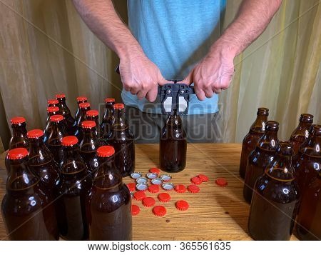 Craft Beer Brewing At Home, Man Closes Brown Glass Beer Bottles With Plastic Capper On Wooden Table 