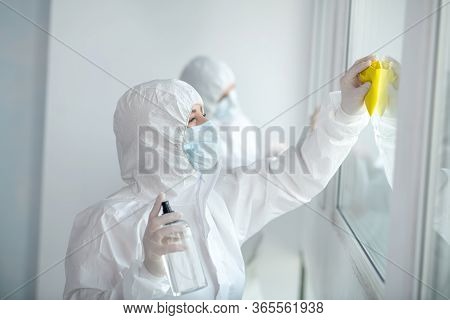 Medical Workers In Protective Clothing And Medical Masks Cleaning And Disinfecting Window Panes