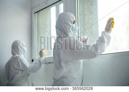 Medical Workers In Protective Clothing And Medical Masks Disinfecting Window
