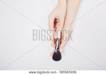 Girl Hand Hold White Brushes Makeup On White Background. Top View Flat Lay