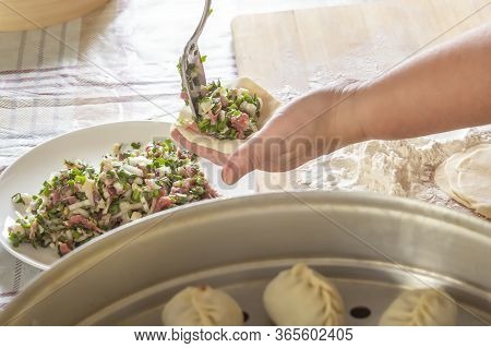 Female Hands Make Manti, Khinkali, Dumplings Or Wonton From Dough With Minced Meat Filling And Green
