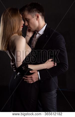 A Young Sexy Couple Gently Embraces Before A Passionate Kiss. A Man In A Strict Suit Carefully Hugs 