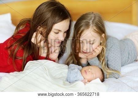 Two Big Sisters Admiring Their Sleeping Newborn Brother. Two Young Girls Holding Their New Baby Boy.