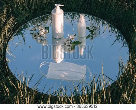 Sanitizers, Mask And Apple Blossoms On The Mirror With A Reflection Of The Skyon The Green Grass