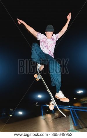 A Young Skatecrack In A Night Skatepark Does A Halfpipe Jump Jump. Youth Culture Leisure Concept At 