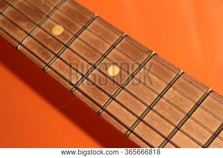 Acoustic Guitar Neck On An Orange Background. Part Of A Guitar On A Bright Background.