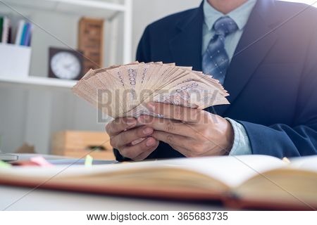 Businessmen Sit Counting Money In Baht In The Office, Preparing To Distribute Salaries And Bonuses O