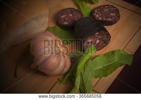 An Argentinian Black Pudding With Arugula, Garlic And Bread On A Wooden Table