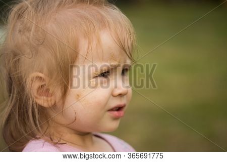 Portrait Of A Baby Girl Close-up. The Child's Face Is Smeared With Sand.