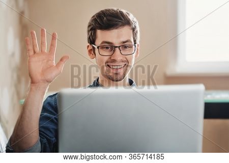 Cheerful Young European Man Doing 'hello' Gesture To Webcamera During Online Conference At Home. Hap