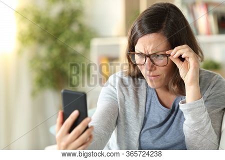 Adult Woman With Eyesight Problems Wearing Eyeglasses Reading On Smart Phone Sitting On A Couch At H