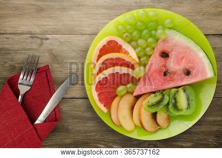 Sliced Fruit On A Borwn Wooden Background. Sliced Fruit On A Light Green Plate Wit Fruits On A Purpl