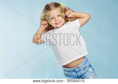 A Child With A Candy. Little Girl With A Round Candy In The Studio On A Blue Background.