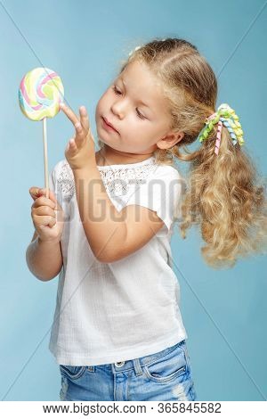 A Child With A Candy. Little Girl With A Round Candy In The Studio On A Blue Background.
