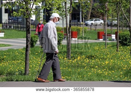 Moscow, Russia - May 2020: Elderly Man In A Medical Mask And Gloves Walks With A Cane In A City Park
