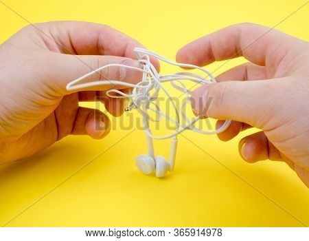 Man Untangles Headphones, On A Yellow Background. Close Up.
