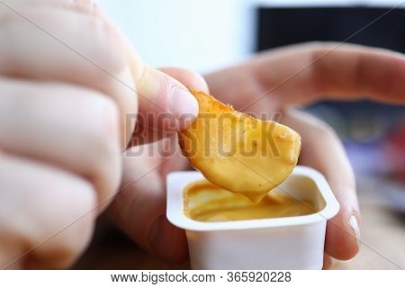 Close-up Of Persons Hand Dipping Fried Potato In Tasty Cheese Sauce. Yummy Snack For Quick Break In 