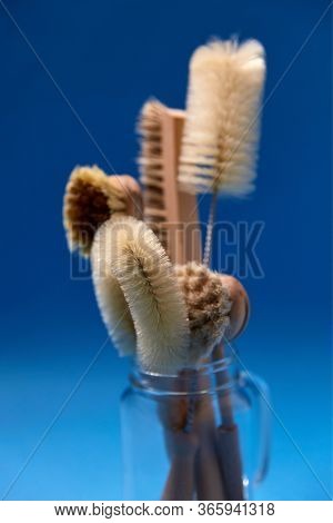 cleaning stuff, sustainability and eco living concept - different brushes with natural bristle and wooden handles in glass jar on blue background