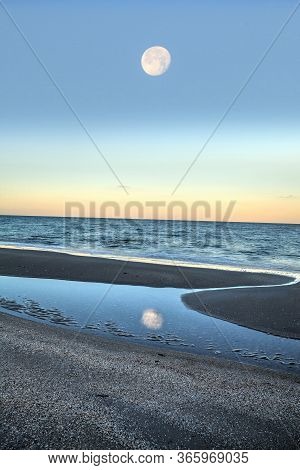 Reflection Of The Full Moonset In A Tidal Pool In Front Of The Ocean On Naples Beach In Naples, Flor