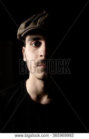Portrait Of Cute Young Guy With Moustache And A Hat On Black, Dark Background.