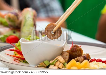 Close Up Of Chopsticks Holding Namnueng Piece While Dip Sauce In White Bowl