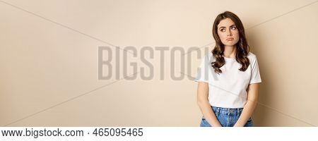 Sad And Tired Brunette Woman Looking Drained And Unamused, Standing With Pokerface Against Beige Bac
